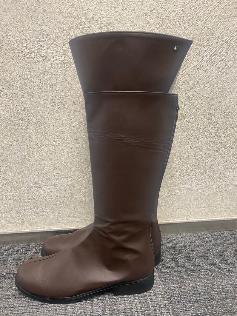 May include: A pair of brown knee-high boots with a zipper on the side. The boots have a pointed toe and a low heel.