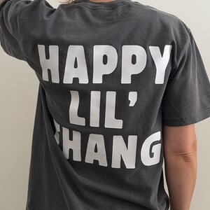 May include: A dark gray t-shirt with white text that reads "HAPPY LIL' HANG" on the back.
