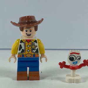 May include: Two Lego figures: Woody, a cowboy with a brown hat, yellow shirt, blue trousers, and a sheriff's badge, and Forky, a white figure with red arms and a fork-like head. The figures are on a white surface.