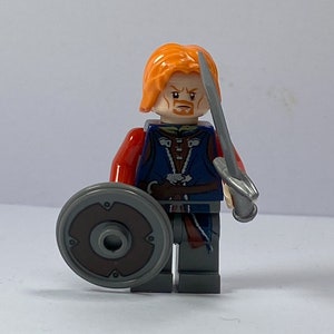 May include: A Lego minifigure of a man with orange hair, a red and blue shirt, a brown belt, and a grey shield and sword.