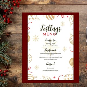 May include: A white Christmas menu with a red border. The menu features a festive design with gold baubles and snowflakes. The menu includes a list of dishes for a holiday meal, including starters, main courses, and desserts. The text on the menu is in German.