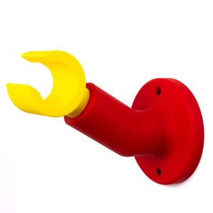 Op de afbeelding: Een aan de muur gemonteerde houder van rood en geel plastic. Het heeft een cirkelvormige basis met drie schroefgaten, een rode schuine arm en een gele, gebogen grijprand. Het ontwerp is eenvoudig en modern, geschikt voor diverse doeleinden.