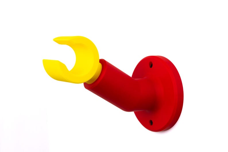 Op de afbeelding: Een aan de muur gemonteerde houder van rood en geel plastic. Het heeft een cirkelvormige basis met drie schroefgaten, een rode schuine arm en een gele, gebogen grijprand. Het ontwerp is eenvoudig en modern, geschikt voor diverse doeleinden.