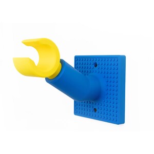 May include: A blue and yellow wall-mounted Lego hand. The hand is yellow and extends from a blue arm and a blue square base with Lego-style studs. The base has two holes for mounting.
