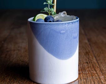 May include: A blue and white ceramic mug filled with ice, blueberries, and a lime wedge. A gold straw sticks out of the top of the mug.