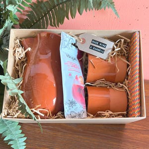 May include: A sangria-making gift set in a wooden box. It features a terracotta pitcher, two terracotta cups, a sangria mix packet, and a tag saying "Make Mine A Sangria". A colourful straw is included.