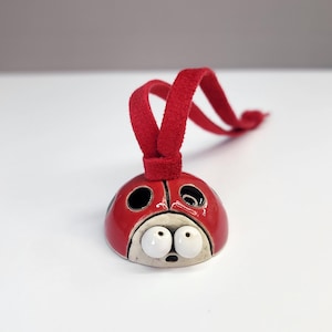 May include: A ceramic ladybug ornament with a glossy red finish and black spots. The ladybug has large, expressive eyes and a red loop for hanging. A whimsical, decorative item.