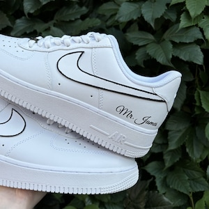 May include: White leather sneakers with a black Nike swoosh and the text "Mr. James" written on the side.