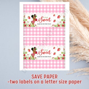 May include: Two printable labels with a pink and white gingham pattern. Each label features a cartoon illustration of a Black baby girl holding a strawberry. The text on the label reads "A Berry Sweet Baby is on the Way!"