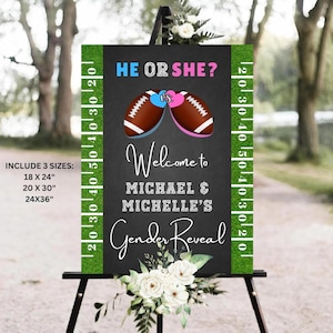 May include: A gender reveal sign on a black chalkboard background, featuring two footballs, one blue and one pink, with the text "He or She?" and "Welcome to Michael & Michelle's Gender Reveal." The sign is framed with green turf and white yard lines.