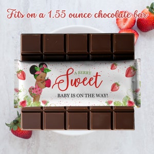 May include: A white chocolate bar wrapper with a red strawberry design and the text "A BERRY Sweet BABY IS ON THE WAY!"  The wrapper is on top of a 1.55 ounce chocolate bar.