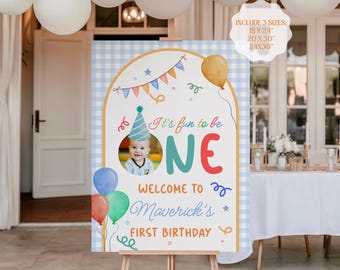 May include: A personalized birthday welcome sign on an easel. The sign features a photo of a baby, the words "It's fun to be ONE", and "Welcome to Maverick's First Birthday". Includes sizes 18x24", 20x30", and 24x36".