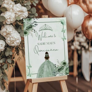 Puede incluir: Un letrero de bienvenida para la Quincea&ntilde;era de Sadie Mae, con una escritura elegante y un dibujo de una ni&ntilde;a con un vestido verde. El letrero est&aacute; decorado con elementos florales y mariposas en tonos verdes, exhibido en un caballete de madera.