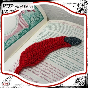 May include: A red and grey knitted bookmark shaped like a bird. The bookmark is lying on top of an open book.