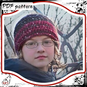 May include: A young person wearing a red, black, and white crocheted hat with a black and white pattern. The person is wearing glasses and has long brown hair.