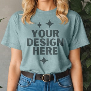 以下が含まれることがあります： 短い袖とクルーネックの薄い青色のTシャツ。シャツには、黒い文字で「YOUR DESIGN HERE」と4つの小さなダイヤモンドの形が前面に印刷されています。