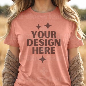 May include: A coral colored t-shirt with short sleeves and a crew neck. The shirt has the text "YOUR DESIGN HERE" printed on the front in brown.