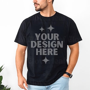 Peut inclure: Un t-shirt noir avec un motif blanc qui dit "YOUR DESIGN HERE" en caractères gras. Le t-shirt est porté par une personne avec une barbe.