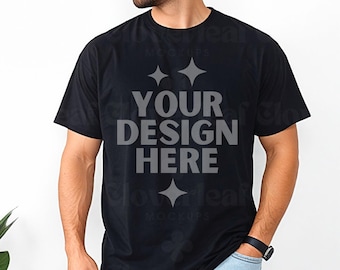 Op de afbeelding: Een zwart T-shirt met een wit ontwerp waarop in vetgedrukte letters "YOUR DESIGN HERE" staat. Het shirt wordt gedragen door een persoon met een baard.