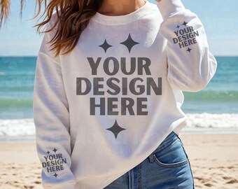 Könnte beinhalten: Weißer Langarm-Sweatshirt mit dem Text "YOUR DESIGN HERE" auf der Vorderseite. Der Sweatshirt hat einen Rundhalsausschnitt und wird von einem Model in blauen Jeans-Shorts getragen. Das Model steht an einem Sandstrand.