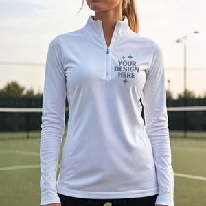 May include: White long-sleeve athletic shirt with a quarter-zip collar. The shirt features the text "YOUR DESIGN HERE" in gray. The shirt is designed for athletic activities and is made of a lightweight material.