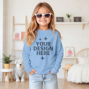 Op de afbeelding: Een lichtblauw longsleeve sweatshirt met de tekst "YOUR DESIGN HERE" in donkergrijs. Het sweatshirt heeft een ronde hals en is versierd met vier kleine grijze sterren.