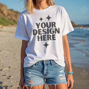May include: A white t-shirt with a black graphic that says "YOUR DESIGN HERE" with stars on either side of the text. The shirt is being worn by a person on a beach.