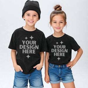 May include: Two children wearing black t-shirts with the text "YOUR DESIGN HERE" in gray. The boy wears a black beanie and the girl has her hair in a bun. Both are smiling and wearing denim shorts.