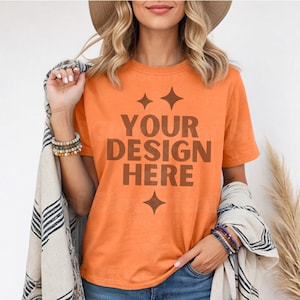 May include: Orange short-sleeved t-shirt with the text "YOUR DESIGN HERE" in brown lettering. The shirt has a relaxed fit and a crew neck.