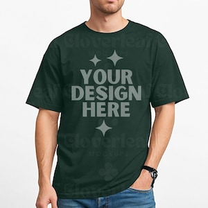 May include: Dark green t-shirt with the text "YOUR DESIGN HERE" in gray. The shirt is a solid color and has a classic crew neck design. The model is wearing a black watch and blue jeans.