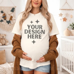 May include: Cream-colored t-shirt with the text "YOUR DESIGN HERE" in gray, accented by star shapes. A brown knitted cardigan is draped over the shoulders. The model is wearing denim shorts.