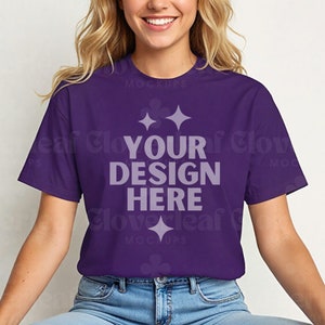 May include: A purple t-shirt with the text "YOUR DESIGN HERE" in white. The shirt is being modeled by a person with long blonde hair.