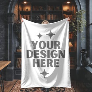 Puede incluir: Una manta blanca con el texto "YOUR DESIGN HERE" en gris. La manta se muestra frente a una estantería y un gato negro. La manta tiene un aspecto suave, ideal para añadir un toque personalizado a cualquier espacio.