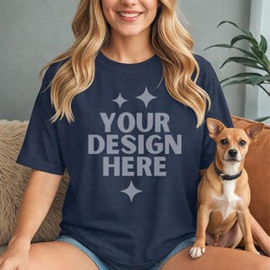 May include: Navy blue t-shirt with the text "YOUR DESIGN HERE" in gray. The shirt is worn by a person. A small brown dog with a black collar sits next to the person.