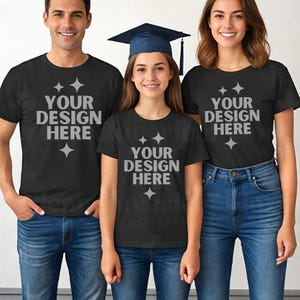 Può includere: Tre persone indossano magliette nere e jeans blu. Le magliette hanno la scritta "YOUR DESIGN HERE" in argento. Una persona al centro indossa un cappello di laurea. L'immagine è un mockup per abbigliamento personalizzato.