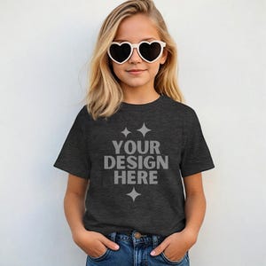 May include: A dark heather grey t-shirt with short sleeves and a crew neck. The shirt has the text "YOUR DESIGN HERE" printed on the front in a light grey color.