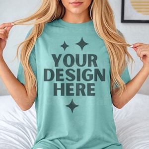 May include: A light blue t-shirt with the text "YOUR DESIGN HERE" in dark gray. The shirt has two small stars above the text and one below.