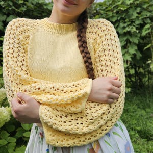 May include: A yellow knitted sweater with a loose fit and openwork sleeves. The sweater has a round neckline and is made of a soft, lightweight yarn.