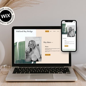 May include: A laptop computer displaying a website with the text "Oakland Bay Bridge" and a photo of a woman wearing sunglasses. The website also includes the text "Hey there" and "News". A mobile phone displaying the same website is in the background.