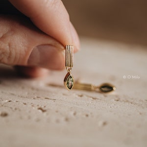 Può includere: Un paio di orecchini d'oro con una pietra preziosa verde appesa a ciascuno. Gli orecchini hanno un design verticale e rigato.
