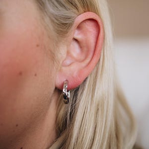 May include: A close-up of a person's ear with a silver hoop earring. The earring has a textured, hammered design.
