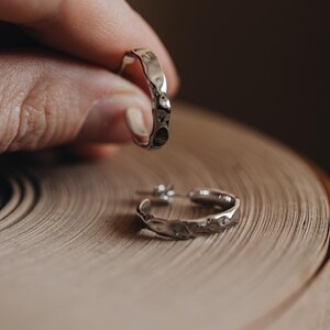 May include: A pair of silver hoop earrings with a textured, hammered finish. The earrings are shown on a wooden surface.