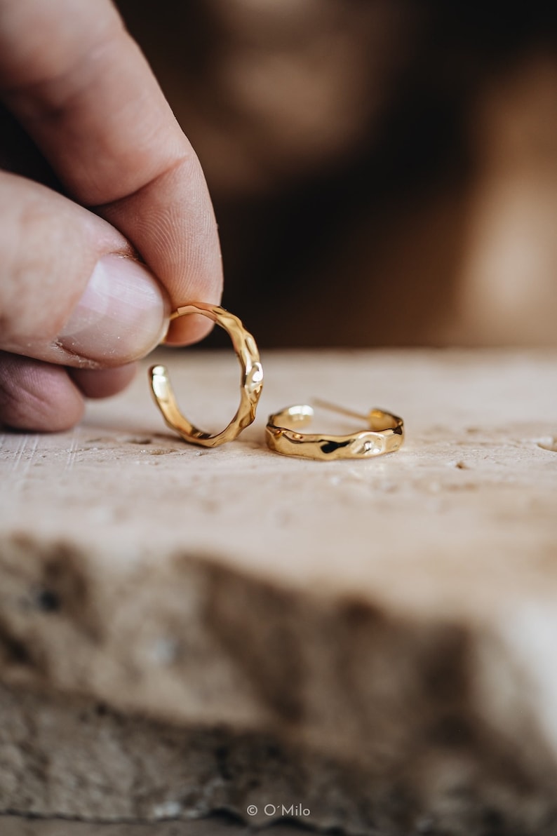 May include: Two gold hoop earrings with a hammered texture. The earrings are small and delicate.