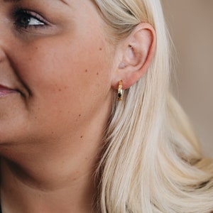 May include: A close-up of a woman's ear with a gold hoop earring. The earring is textured and has a slightly hammered finish.
