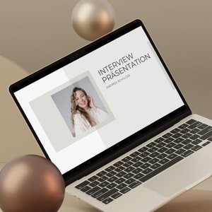 May include: A silver laptop showing a presentation titled "Interview Präsentation" with a photo of a smiling woman. The laptop is on a beige platform with three floating spheres. The laptop's keyboard is black.