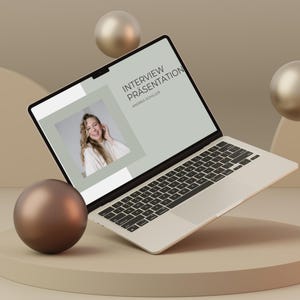 May include: A laptop computer with a white background and a presentation on the screen titled "Interview Presentation" by Andrea Schiller. The laptop is floating above a beige circular platform with three brown spheres around it.