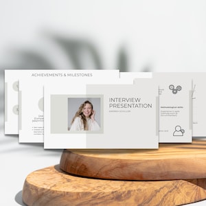 Könnte beinhalten: Eine Präsentation mit dem Titel „Interview Präsentation“ von Andrea Schiller. Die Folien sind weiß mit hellgrauen Akzenten und zeigen ein Foto einer lächelnden Frau. Die Folien werden auf einer Holzoberfläche angezeigt.