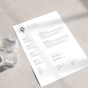 Könnte beinhalten: Eine schwarz-weiße Lebenslaufvorlage mit einem Porträt einer Frau in der oberen linken Ecke. Der Lebenslauf enthält Abschnitte für Berufserfahrung, ehrenamtliche Tätigkeiten, Leistungen, berufliche Entwicklung und Hobbys. Der Text im Lebenslauf ist in einer einfachen, modernen Schriftart.