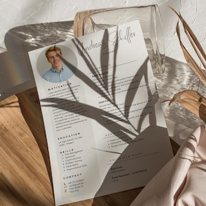 Könnte beinhalten: Ein Lebenslauf mit dem Namen „Andreas Schiller“ oben, mit Abschnitten für Erfahrung, Ausbildung, Fähigkeiten und Kontaktinformationen. Der Lebenslauf liegt auf weißem Papier mit Schatten.