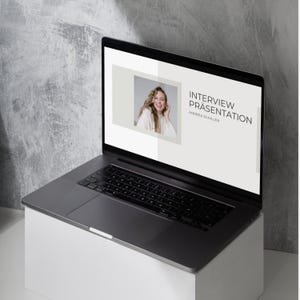 Può includere: Un computer portatile che mostra una presentazione intitolata "Interview Präsentation" con il nome "Andrea Schiller" sotto il titolo. Una donna è raffigurata in un piccolo riquadro sul lato sinistro dello schermo.
